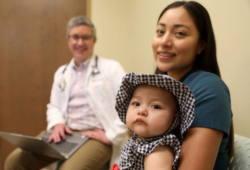 Rifle7021 A mother holding her baby while a doctor in a white coat sits in the background.