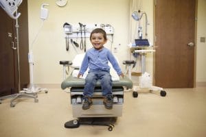 Little Boy Smiling A child is sitting on a medical exam table in a doctor's office, smiling.