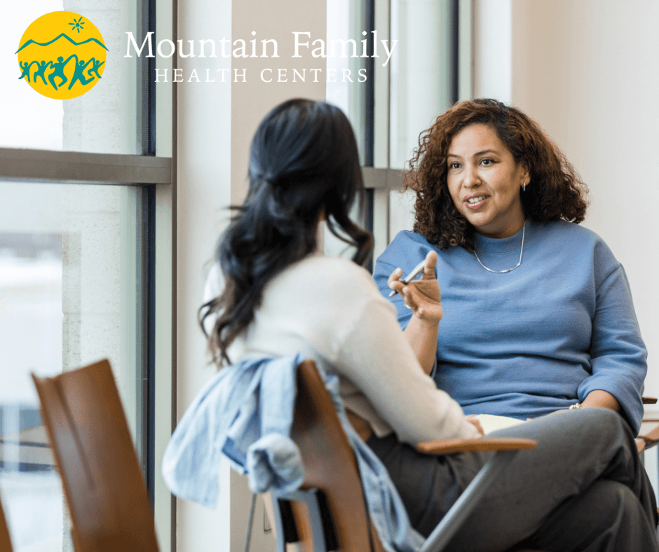 Two people are sitting and having a conversation in a room with chairs, with the logo "Mountain Family Health Centers" visible.