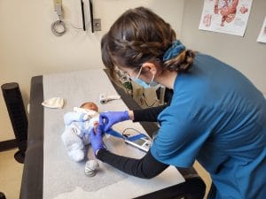 A healthcare professional is examining a baby on a medical table.